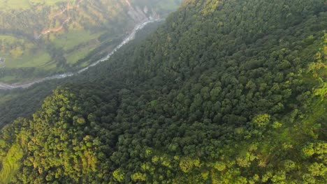 Filmische-Drohnenaufnahme-über-üppig-Grünen-Bergen-Mit-Fluss-Im-Tal-Von-Nepal-Bei-Sonnenuntergang-–-Aufnahme-Von-Oben-Nach-Unten