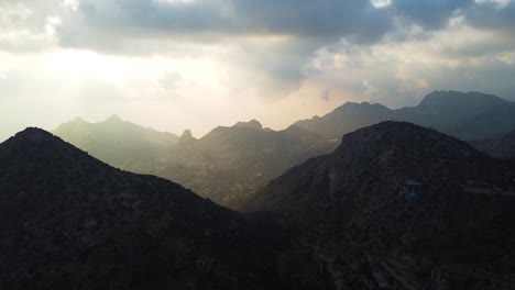 Luftaufnahme-Der-Wunderschönen-Bergkette-In-Saudi-Arabien,-Beleuchtung-Durch-Sonnenstrahlen-Zwischen-Wolken