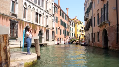 Excited-female-tourist-at-Venetian-canal-edge-smiles-as-gondola-approaches