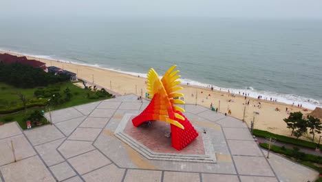 Aerial-orbit-view-capturing-the-beauty-of-beach-monument-adorned-with-various-sand-sculptures
