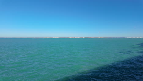 Die-Weitläufige-Bucht-Von-Cádiz,-Von-Einem-Strandweg-Aus-Betrachtet,-Mit-Ruhigem-Türkisfarbenem-Wasser,-Das-Am-Horizont-Auf-Den-Klaren-Blauen-Himmel-Trifft