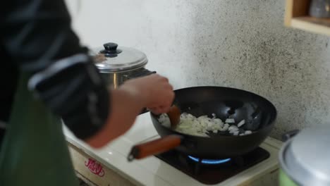 Freshly-cut-onions-fried-in-black-fry-pan-and-stirred-by-hand-with-wooden-spoon,-filmed-as-closeup-slow-motion-style-shot