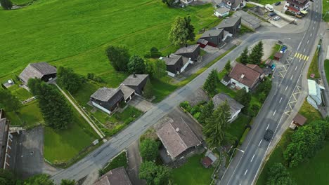 Aerial-view-of-a-car-driving-on-any-empty-street-in-a-quiet-neighborhood,-lined-with-family-homes-on-a-field-of-lush-green-grass-and-trees