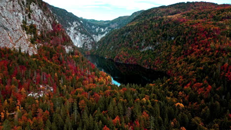 Drone-approaching-an-isolated-mountaintop-lake-surrounded-by-leaves-changing-color