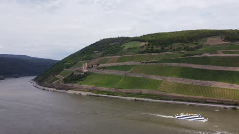Pleasure-boat-cruise-by-Ehrenfels-Castle-on-river-Rhine,-Static-Aerial