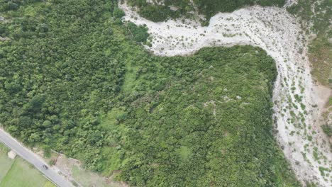 Flying-over-green-forest-near-highway-traffic-and-dry-riverbed,-Albania