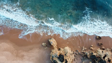 Drone-shot-of-rocky-beach-with-waves-breaking-into-the-sand