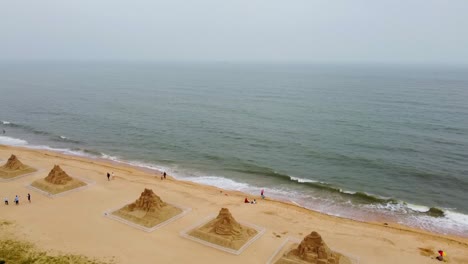 Aerial-forward-dolly-view-of-beach,-flying-over-several-sand-sculptures,-foggy-day-in-Nanhai,-China