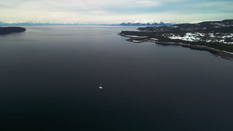 Sailboat-in-middle-of-snowy-Islands,-partly-sunny-spring-day-in-Alaska,-USA---Aerial-view