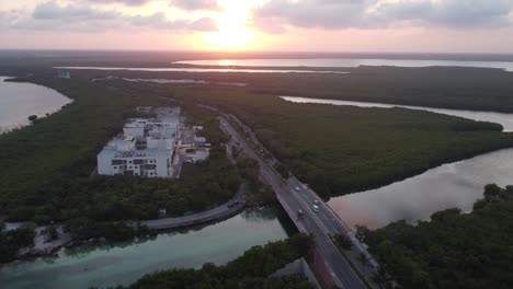 Sunset-aerial-drone-shot-over-Punta-Nizuc-bridge-by-the-Nichupte-lagoon-in-Cancun-Mexico,-surrounded-by-river-systems-and-greenery