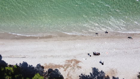 A-high-angle-drone-shot-moves-right-along-a-beach-as-a-family-plays-in-the-water
