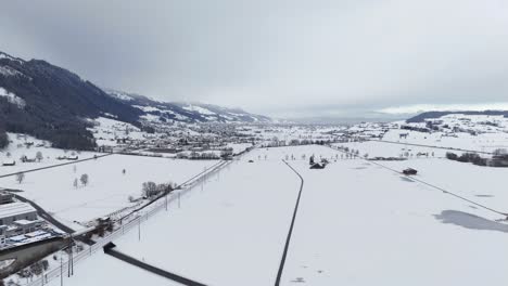 Aerial-approaching-shot-snowy-winter-landscape-in-Switzerland-and-riding-train-on-track