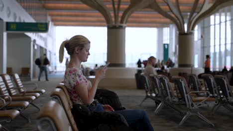 Eine-Junge-Dame-Sitzt-In-Der-Flughafenlounge-Und-Schaut-Auf-Ihr-Handy