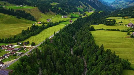 Aerial-view-of-a-village-in-the-Swiss-Alps-in-Lucerne,-surrounded-by-lush-green-trees,-on-a-field-of-grass-at-the-base-of-mountains
