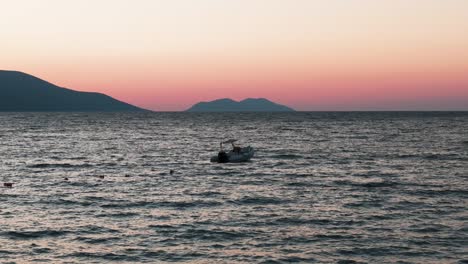 Ruhige-Aussicht-Auf-Ein-Schwimmendes-Boot-Auf-Dem-Meer-Mit-Einer-Bergsilhouette-In-Sonnenuntergangsfarbe