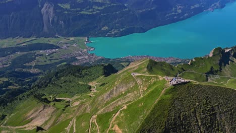 Eine-Luftaufnahme-Einer-Grünen-Bergkette,-Die-Langsam-Einen-Türkisfarbenen-See-Und-Schneebedeckte-Berge-Im-Hintergrund-Enthüllt