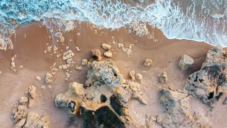 Top-down-drone-movement-shot-of-rocky-beach-with-waves-gentle-breaking-into-the-sand