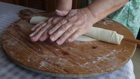 Las-Manos-De-La-Abuela-Amasando-Masa-Para-Pastel-Con-Palo-De-Madera,-Preservando-El-Patrimonio-Culinario-Tradicional.