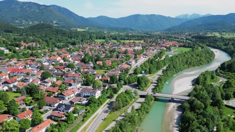 Aerial-view-of-a-suburban-town-nestled-against-mountains-and-surrounded-by-trees,-along-a-river-and-forest-connected-by-a-bridge