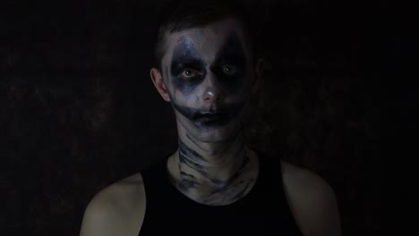 Gruselig-Verrückter-Halloween-Gesichts-Make-up-Kaukasier-Tritt-Vor-Schwarzem-Hintergrund-Auf-Und-Dreht-Den-Kopf,-Während-Er-In-Die-Kamera-Starrt