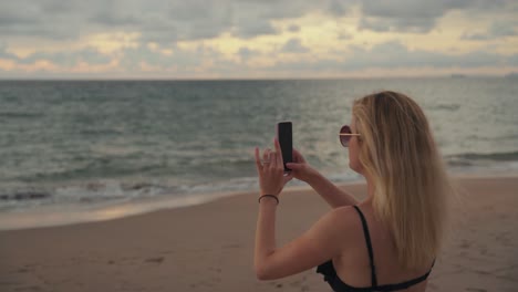 Eine-Junge-Attraktive-Frau-Im-Badeanzug-Macht-Ein-Foto-Mit-Ihrem-Handy-Am-Strand