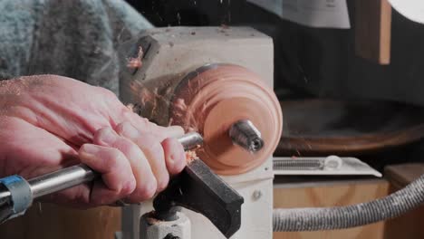 Old-man-using-a-lathe-and-chisel-to-cut-away-wood-and-release-a-metal-grommet