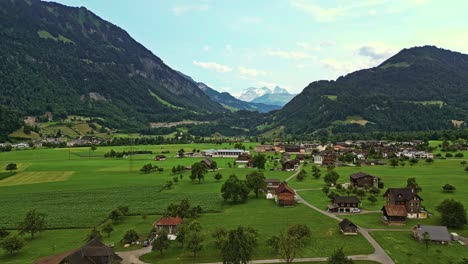 Drone-shot-of-a-small-village-in-the-Swiss-Alps-surrounded-by-forest-mountains,-Switzerland,-Europe