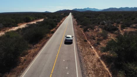 Aerial-of-car-driving-on-a-straight-road-through-desert-landscape