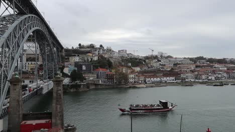 Tourists-on-Rabelo-Boat-almost-crossing-under-Dom-Luis-I-Bridge,-Porto