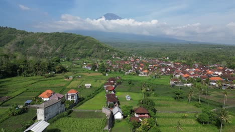 Drone-flying-over-rice-terrace-farm-land-and-a-small-village-with-a-volcano-in-the-background