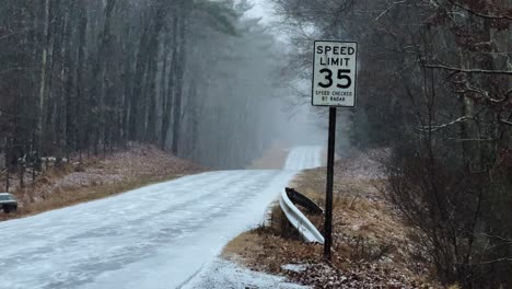 Gentle-slow-motion-snowfall-on-a-forest-road-with-a-speed-limit-sign,-at-the-beginning-of-a-nor'easter-in-America