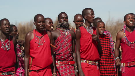 Tribesmen-in-Masaimara,-Kenya-dressed-in-red-dancing-and-singing