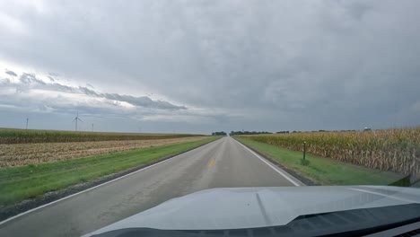 POV---driving-on-a-rural-road-past-farm-yards-and-corn-fields-soon-to-be-harvested-on-a-cloudy-day