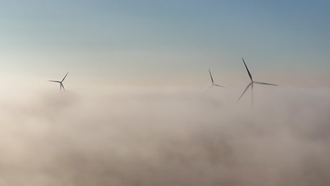 Drohnenansicht-Von-Windmühlen-Bei-Sonnenaufgang,-Während-Tief-Liegender-Nebel-Das-Umliegende-Ackerland-Bedeckt