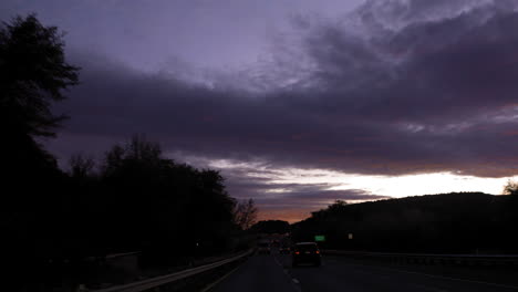 Driving-along-a-dark-highway-at-sunset-with-beautiful-purple-blue-clouds---fpv
