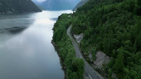 Driving-car-travelling-on-Norwegian-roads-next-to-a-fjord-in-the-wilderness-of-Norway