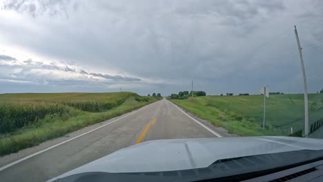 POV---driving-on-a-country-road-past-alfalfa-and-corn-fields-on-a-cloudy,-rainy-day-in-late-summer-in-the-Midwest