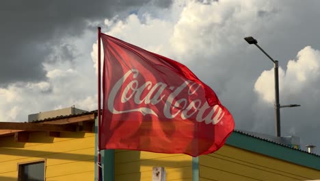 Close-up-of-Coca-Cola-flag-waving-at-sunset-at-a-beach-stand