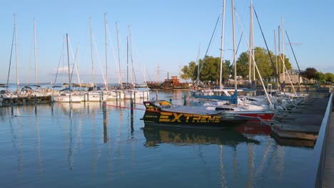 Ungarn,-Balatonfüred-Yachthafen-Mit-Festgemachten-Segelbooten-Und-Ankommendem-Traditionsschiff-Im-Hintergrund