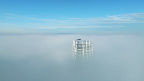 In-aerial-video,-the-drone-orbits-right,-encircling-a-solitary-skyscraper-amid-thick-morning-clouds-on-the-left