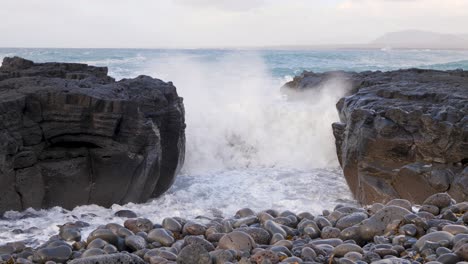 Waves-crashing-against-volcanic-basalt-columns-on-a-pebble-beach-in-Iceland,-creating-a-dramatic-natural-scene