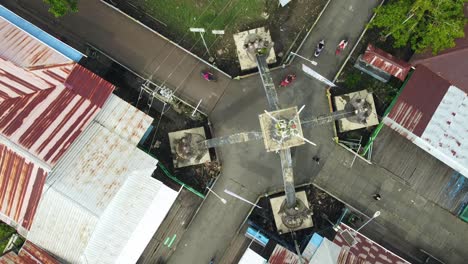 Eine-Drohne-Von-Oben-Zeigt-Ein-Sehr-Großes,-Handförmiges-Denkmal,-Das-Auf-Einer-Tafel-Steht,-Die-Aktivitäten-Der-Menschen-In-Der-Stadt-Agats-Asmat,-Papua