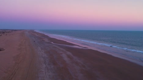 Vast-beach-with-a-purple-sunset-sky-with-paraglider-moving-away
