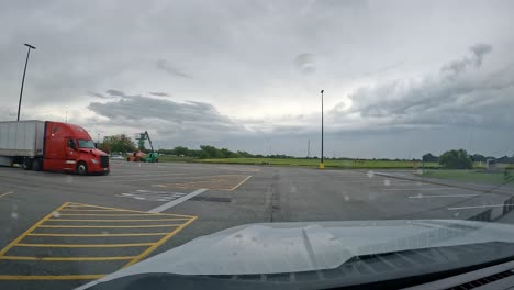 POV---Driving-thru-the-parking-lot-of-Walmart,-past-multiple-shipping-containers-on-a-cloudy,-rainy-day