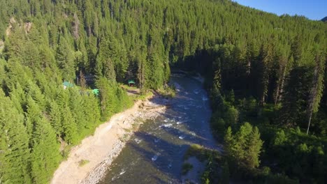 Luftaufnahme-Mit-Blick-Auf-Einen-Atemberaubenden-Blauen-Fluss,-Der-Sich-Dann-Nach-Oben-Neigt-Und-Ein-Grünes-Haus-Enthüllt,-Das-Im-Nördlichen-Wald-Kanadas-In-British-Columbia-Versteckt-Ist