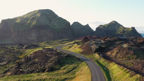 Winding-road-through-green-covered-hills-and-rugged-terrain-of-the-Westman-Islands,-with-a-clear-sky-at-daybreak