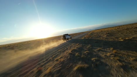 Niedrige-Filmische-Luftaufnahmen-Folgen-Einem-Geländewagen,-Der-Auf-Einer-Malerischen-Unbefestigten-Wüstenstraße-In-Utah-In-Den-Sonnenuntergang-Fährt