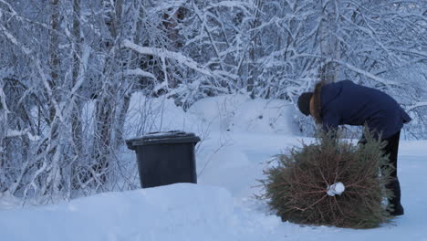 man-dragging-used-fir-Christmas-tree-out-into-the-trash-can