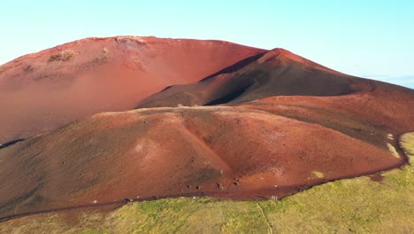 Aerial-view-of-the-vibrant-red-volcanic-cone-Westman-in-Iceland,-with-contrasting-green-grass-at-its-base