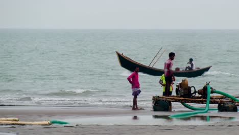 Boat-passing-by-and-people-watching-on-Kuakata-beach-in-Kuakata,-Bangladesh